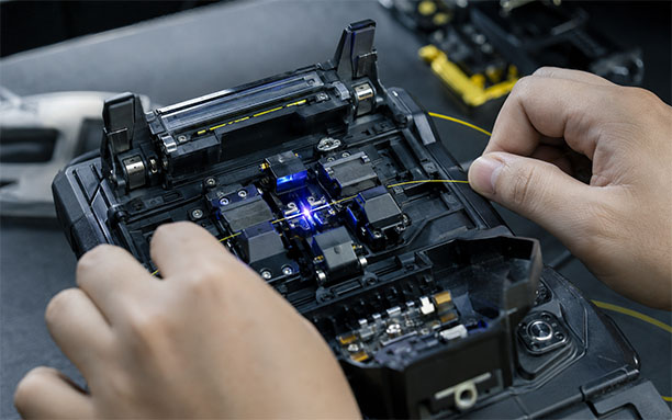 Technician performing fusion splicing on single-mode fiber with electric arc visible